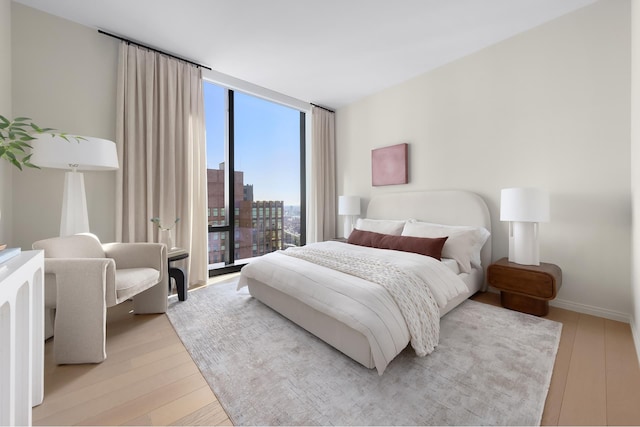 bedroom with a wall of windows, baseboards, light wood-style flooring, and a view of city