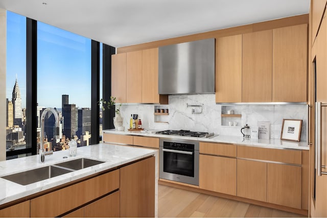 kitchen featuring light stone counters, appliances with stainless steel finishes, wall chimney exhaust hood, and a sink