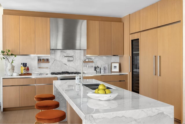 kitchen featuring paneled fridge, light stone counters, wall chimney exhaust hood, and tasteful backsplash