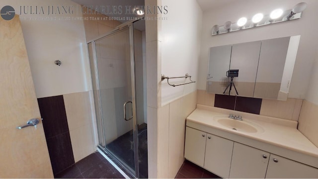 bathroom featuring tile patterned flooring, tile walls, a shower with shower door, and vanity