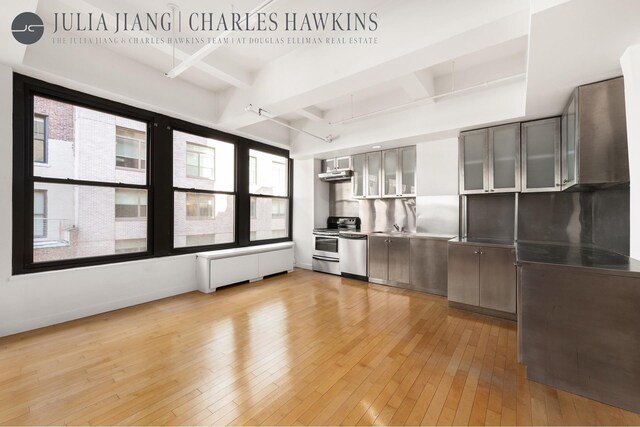 315 W 36th St Unit 12B, New York City, NY 10018 - kitchen featuring appliances with stainless steel finishes, beam ceiling, plenty of natural light, light wood finished floors, and glass insert cabinets