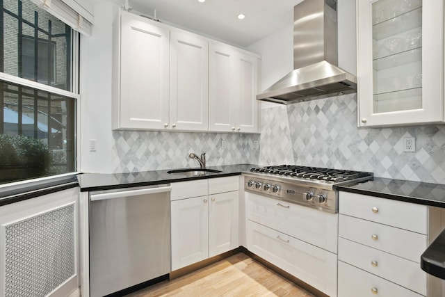 kitchen with wall chimney range hood, dark countertops, a sink, and appliances with stainless steel finishes