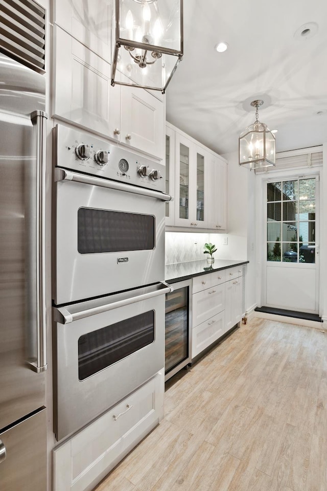 kitchen with wine cooler, high end fridge, light wood-style floors, double oven, and a notable chandelier