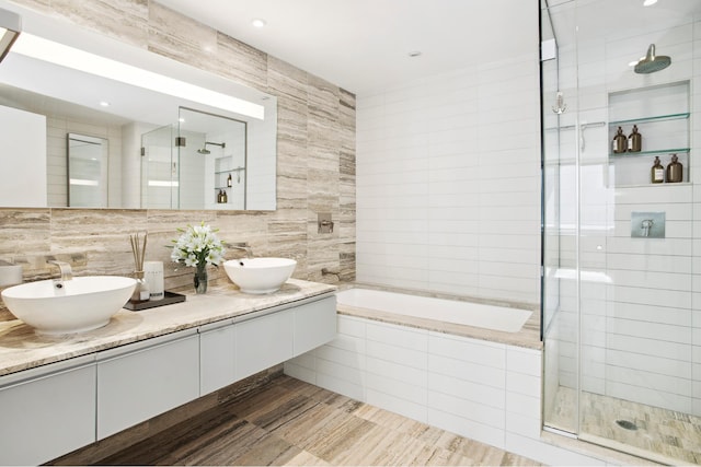 322 W 57th St Unit 55S1, New York City, NY 10019 - full bathroom featuring tile walls, a shower stall, tiled tub, double vanity, and decorative backsplash