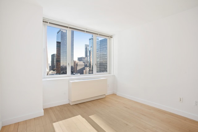 322 W 57th St Unit 55S1, New York City, NY 10019 - spare room with wood finished floors, radiator heating unit, and a skyline view
