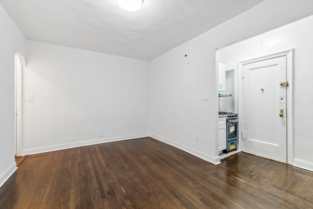 empty room featuring baseboards, arched walkways, and dark wood-style flooring