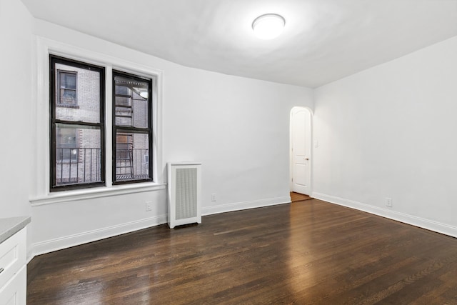 empty room featuring dark wood-type flooring, arched walkways, and baseboards