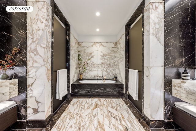bathroom with a garden tub, stone wall, recessed lighting, and marble finish floor