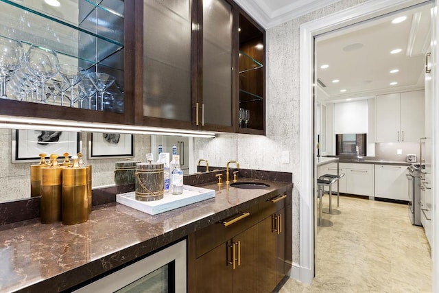 bar with dark stone countertops, ornamental molding, white cabinets, dark brown cabinetry, and sink