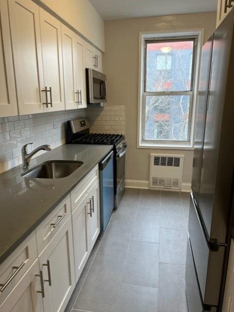 kitchen with stainless steel appliances, a sink, white cabinetry, and radiator