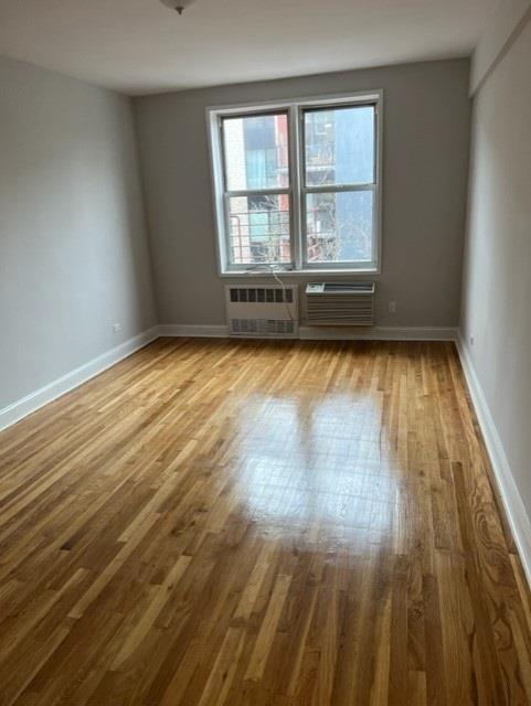 spare room featuring light wood-type flooring, baseboards, radiator heating unit, and a wall mounted AC