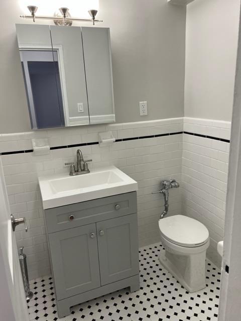 bathroom with toilet, wainscoting, tile walls, and vanity