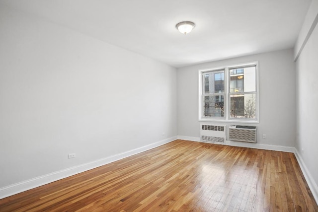 empty room featuring radiator, light wood-style flooring, baseboards, and a wall mounted AC