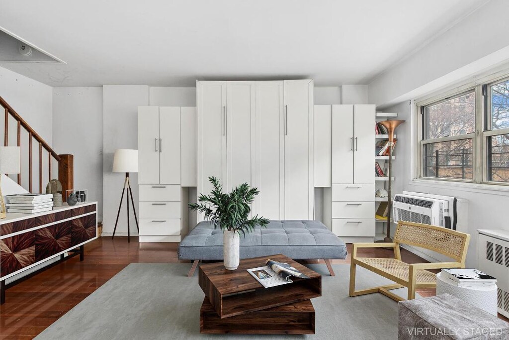 living area with stairs, dark wood-style flooring, radiator heating unit, and a wall mounted air conditioner