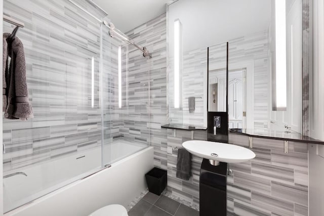 bathroom featuring combined bath / shower with glass door, tile patterned floors, tile walls, and toilet