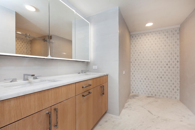 full bath featuring a tile shower, a sink, tile walls, and double vanity