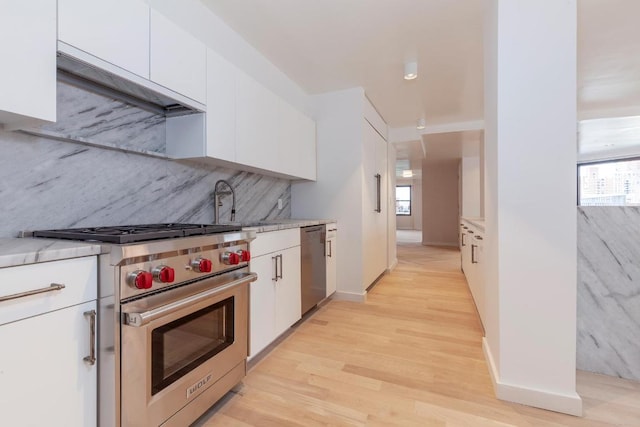 kitchen with appliances with stainless steel finishes, white cabinetry, tasteful backsplash, light hardwood / wood-style floors, and sink