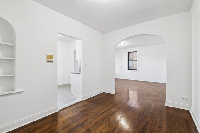 spare room with dark wood-type flooring and built in shelves