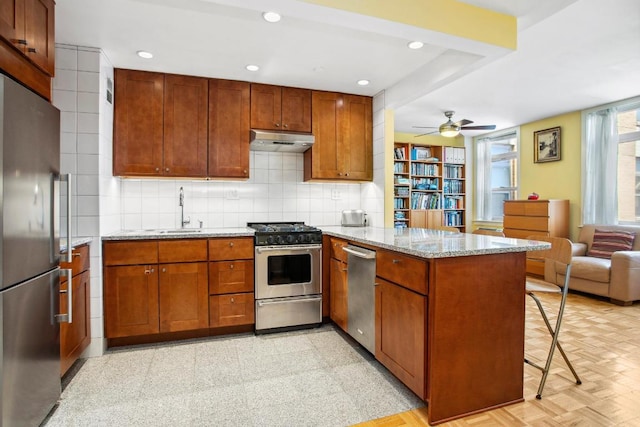 kitchen with sink, appliances with stainless steel finishes, kitchen peninsula, light stone countertops, and backsplash