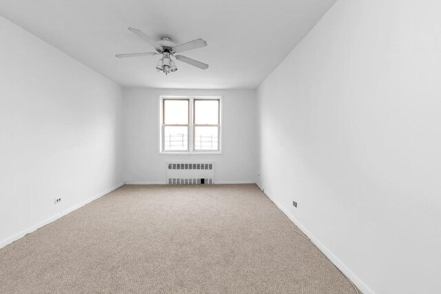 carpeted spare room with ceiling fan and radiator