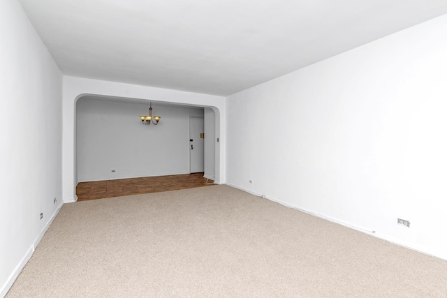 carpeted spare room featuring arched walkways and an inviting chandelier