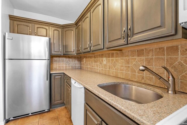 kitchen featuring white dishwasher, light stone countertops, decorative backsplash, stainless steel refrigerator, and sink