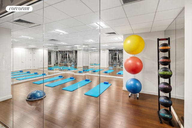 gym with baseboards, visible vents, a drop ceiling, and wood finished floors