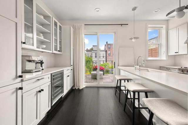 kitchen featuring a kitchen bar, decorative light fixtures, wine cooler, white cabinets, and sink