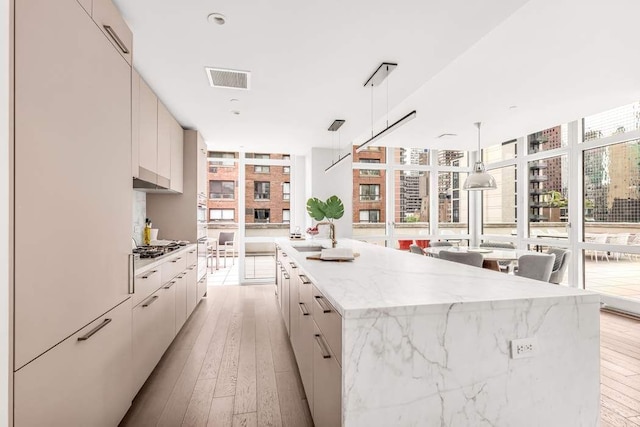 kitchen featuring sink, hanging light fixtures, floor to ceiling windows, light hardwood / wood-style floors, and a large island with sink