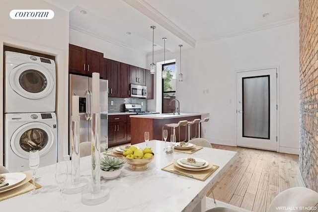 kitchen featuring appliances with stainless steel finishes, decorative light fixtures, backsplash, stacked washer and clothes dryer, and a kitchen island with sink