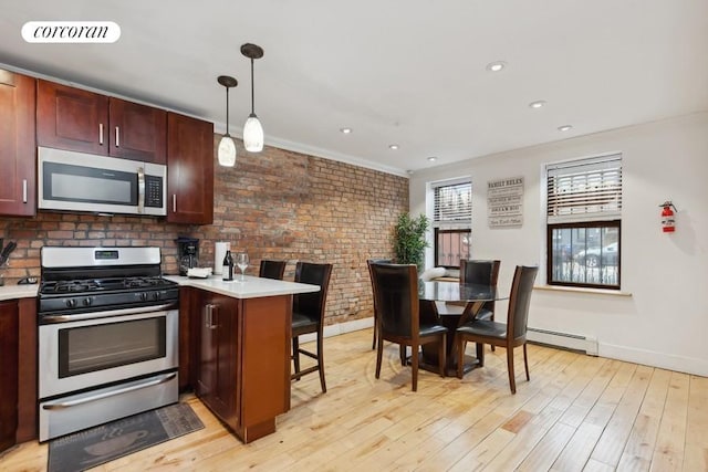 kitchen featuring decorative light fixtures, a kitchen bar, stainless steel appliances, baseboard heating, and brick wall