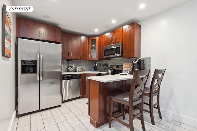 kitchen with appliances with stainless steel finishes, a kitchen bar, tasteful backsplash, sink, and kitchen peninsula