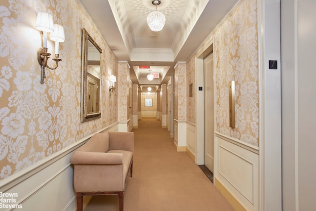 corridor with a tray ceiling, an inviting chandelier, elevator, ornamental molding, and light carpet