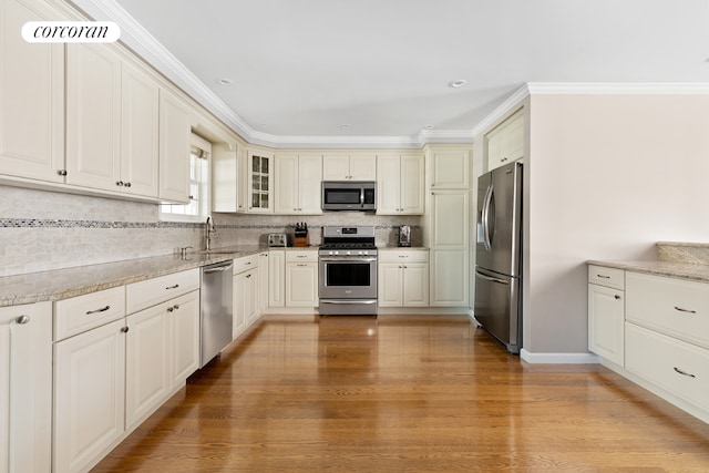 kitchen with sink, light hardwood / wood-style flooring, ornamental molding, appliances with stainless steel finishes, and backsplash