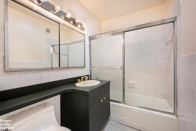 full bathroom featuring bath / shower combo with glass door, tile walls, vanity, toilet, and tile patterned floors