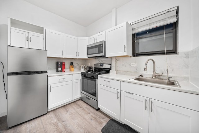 kitchen featuring appliances with stainless steel finishes, white cabinetry, tasteful backsplash, light hardwood / wood-style floors, and sink