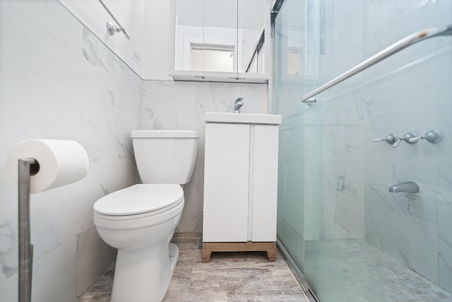 bathroom with an enclosed shower, vanity, tile walls, and toilet