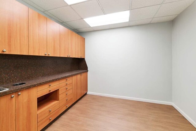 kitchen with dark stone countertops, light hardwood / wood-style flooring, a drop ceiling, and backsplash