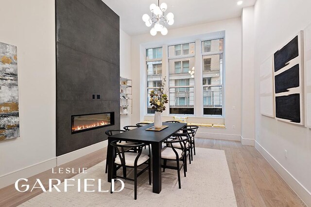 dining space with an inviting chandelier, plenty of natural light, a tiled fireplace, and light wood-type flooring