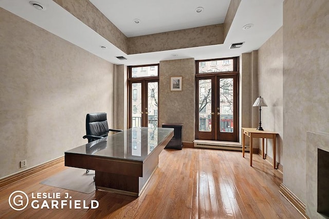 office featuring a raised ceiling, a towering ceiling, light wood-type flooring, and french doors