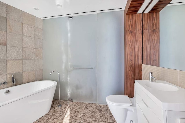 bathroom featuring toilet, a freestanding bath, tile walls, and vanity