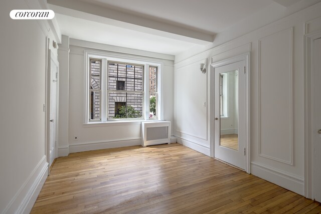 unfurnished room with radiator, beam ceiling, and light hardwood / wood-style floors