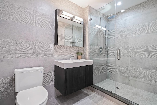 bathroom with toilet, tile walls, a shower with shower door, and vanity