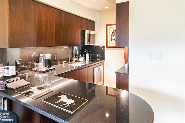 kitchen with modern cabinets, a sink, stainless steel microwave, backsplash, and dark stone counters