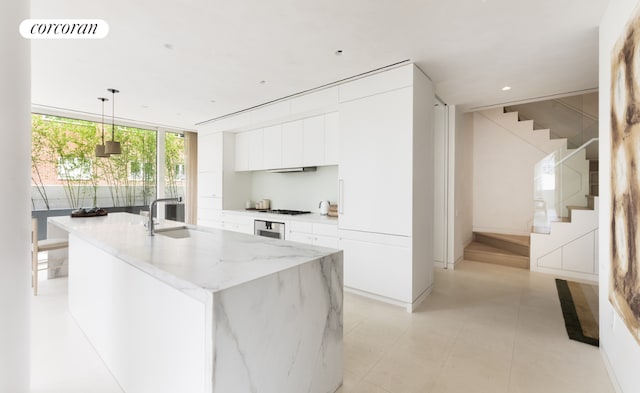 kitchen with sink, hanging light fixtures, expansive windows, white cabinets, and a center island with sink