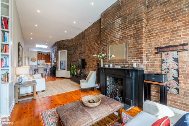 living room with brick wall, hardwood / wood-style floors, and a skylight