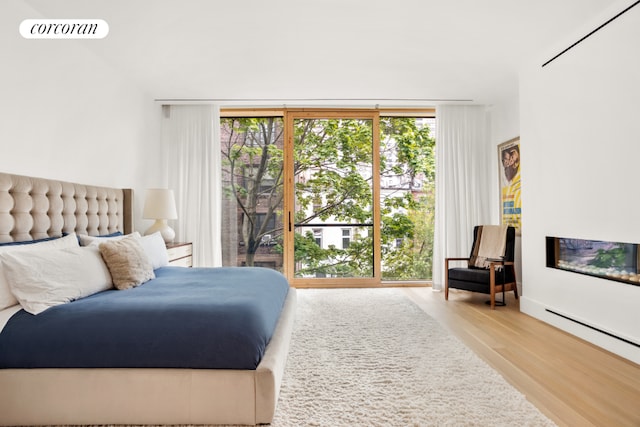 bedroom featuring a baseboard heating unit, a wall of windows, and light hardwood / wood-style flooring