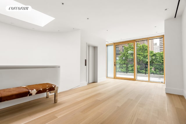 unfurnished room with a wall of windows, a skylight, and light hardwood / wood-style floors