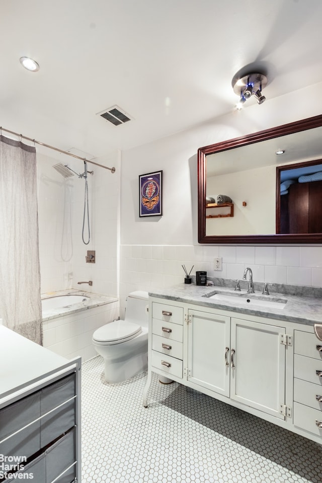 bathroom with toilet, tiled shower / bath combo, vanity, visible vents, and tile walls