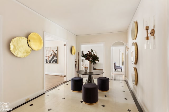 hall featuring tile patterned floors, baseboards, and arched walkways